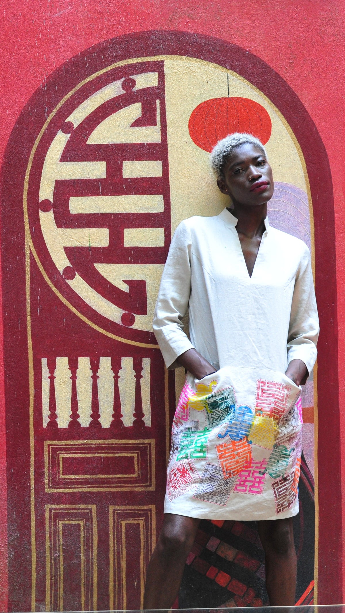 Model in a white tunic hand-painted with coins before a red temple door