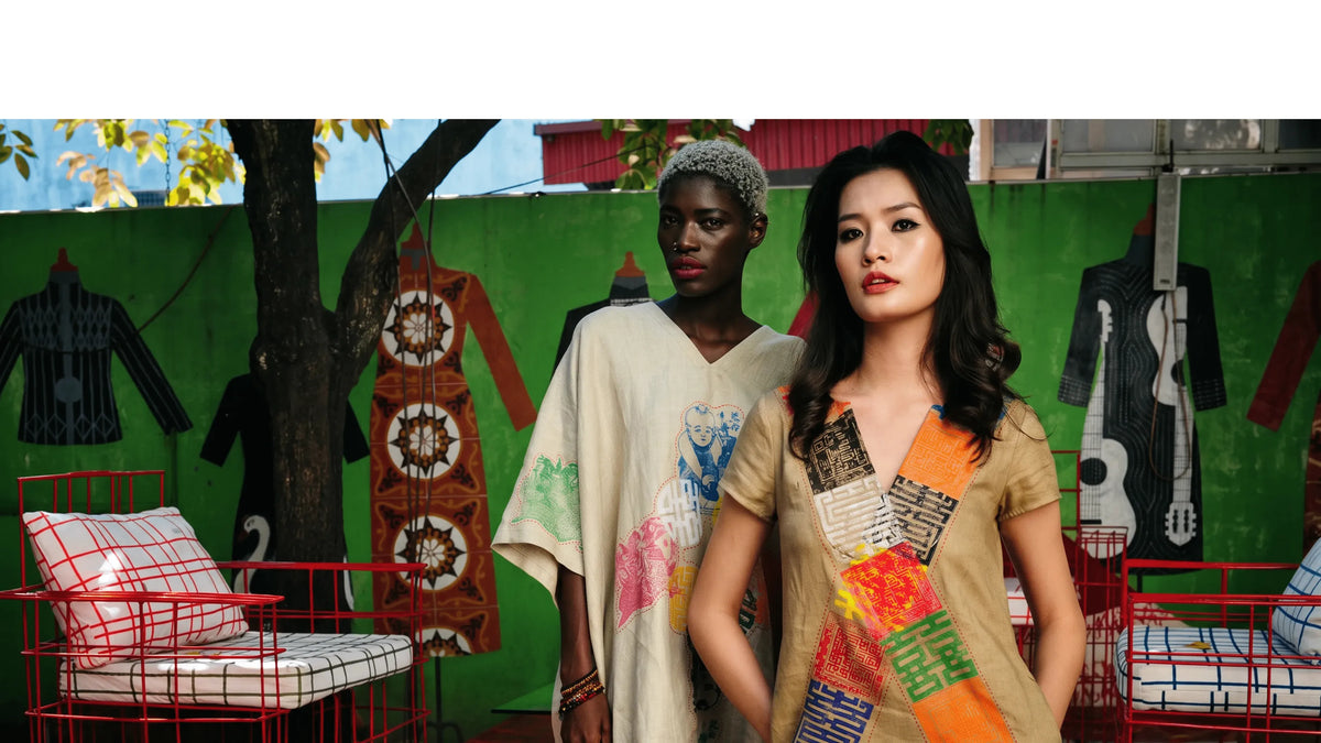Two models in hand-painted patchwork kaftans in a room hung with rugs and guitars