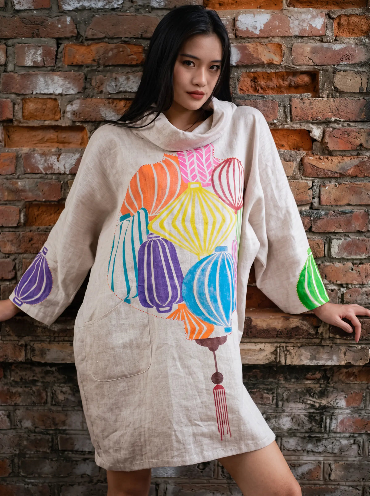 Model in a linen tunic hand-painted with lanterns against a brick wall