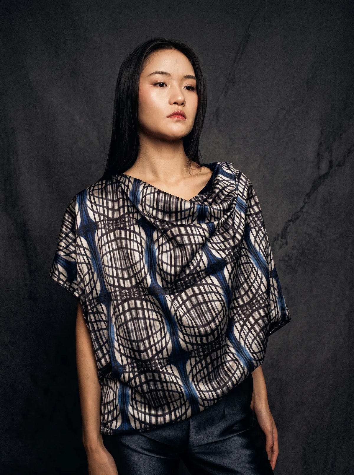 Model in a black and white hand-painted silk top against a dark wall