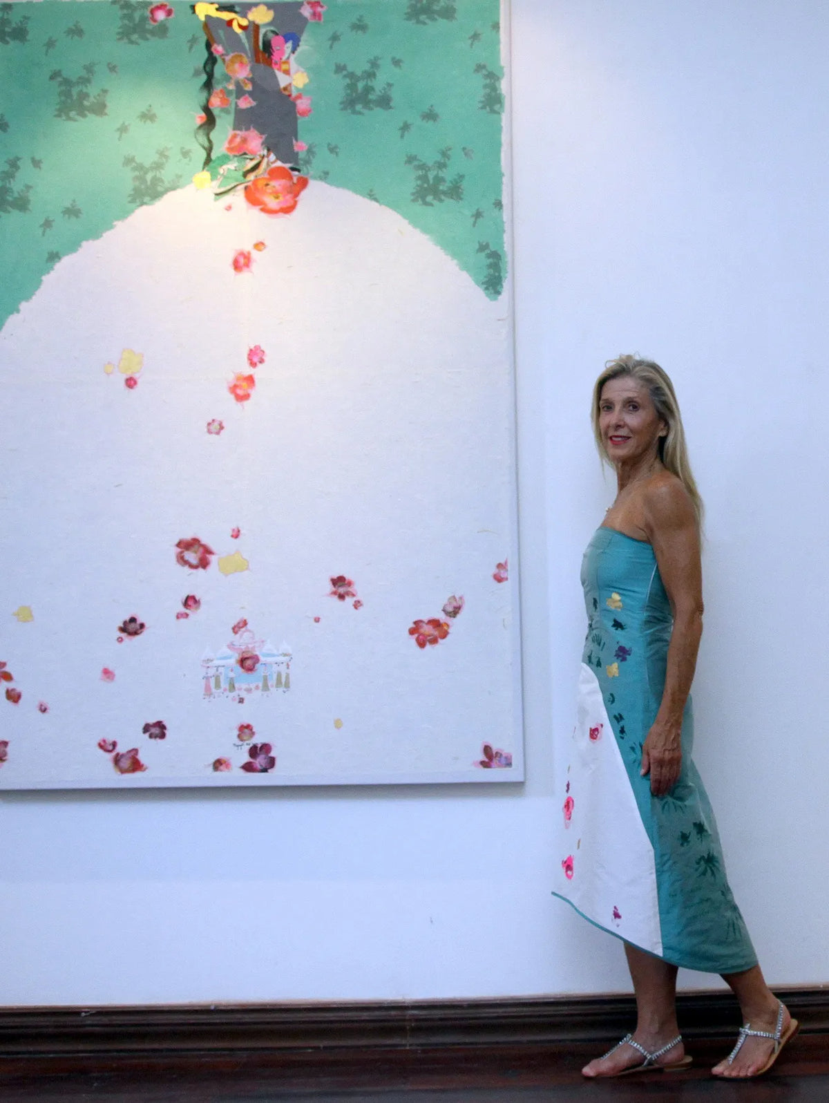 A woman in a turquoise Chula dress beside a painting of falling blossom, 2009