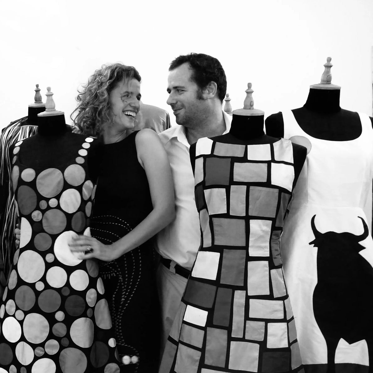 Diego Cortizas and Laura Fontan laughing together among dress forms wearing early Chula pieces, in black and white