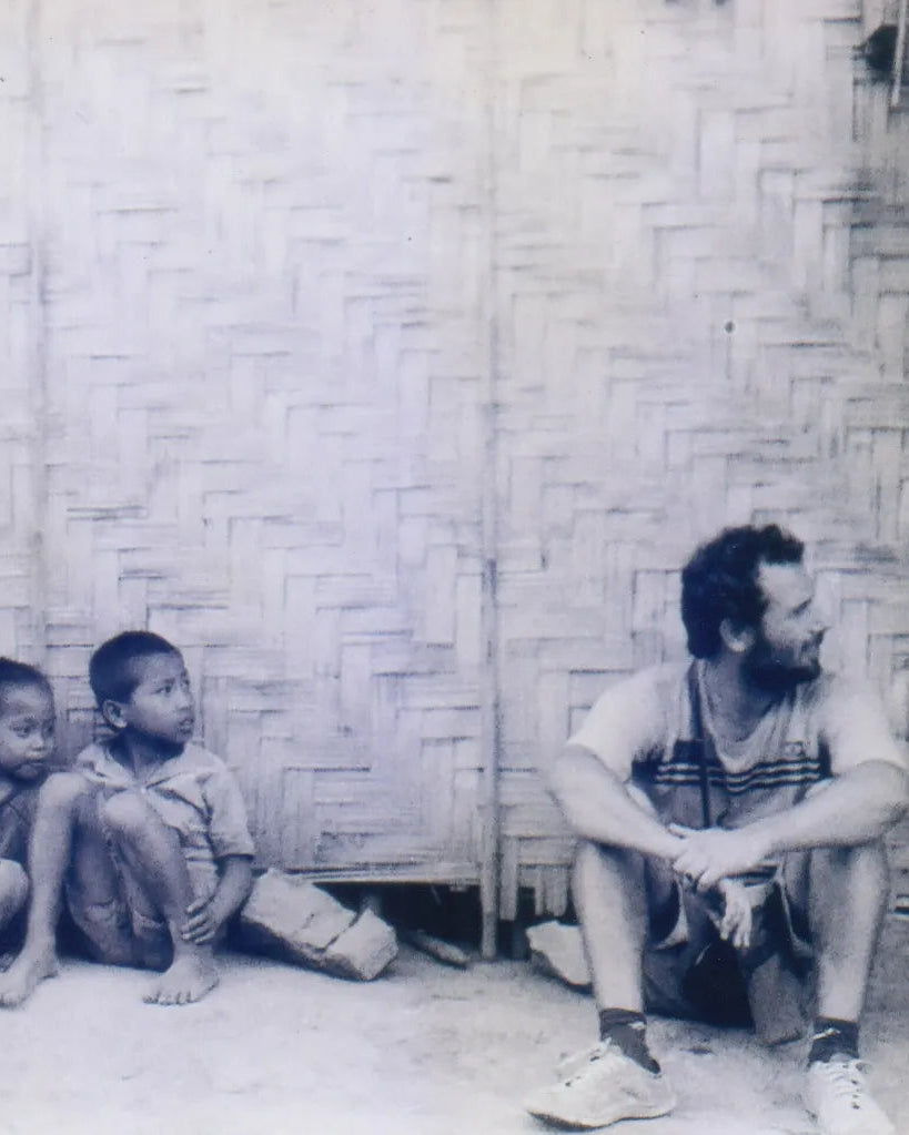 Diego Cortizas sitting with two children against a woven wall in Southeast Asia
